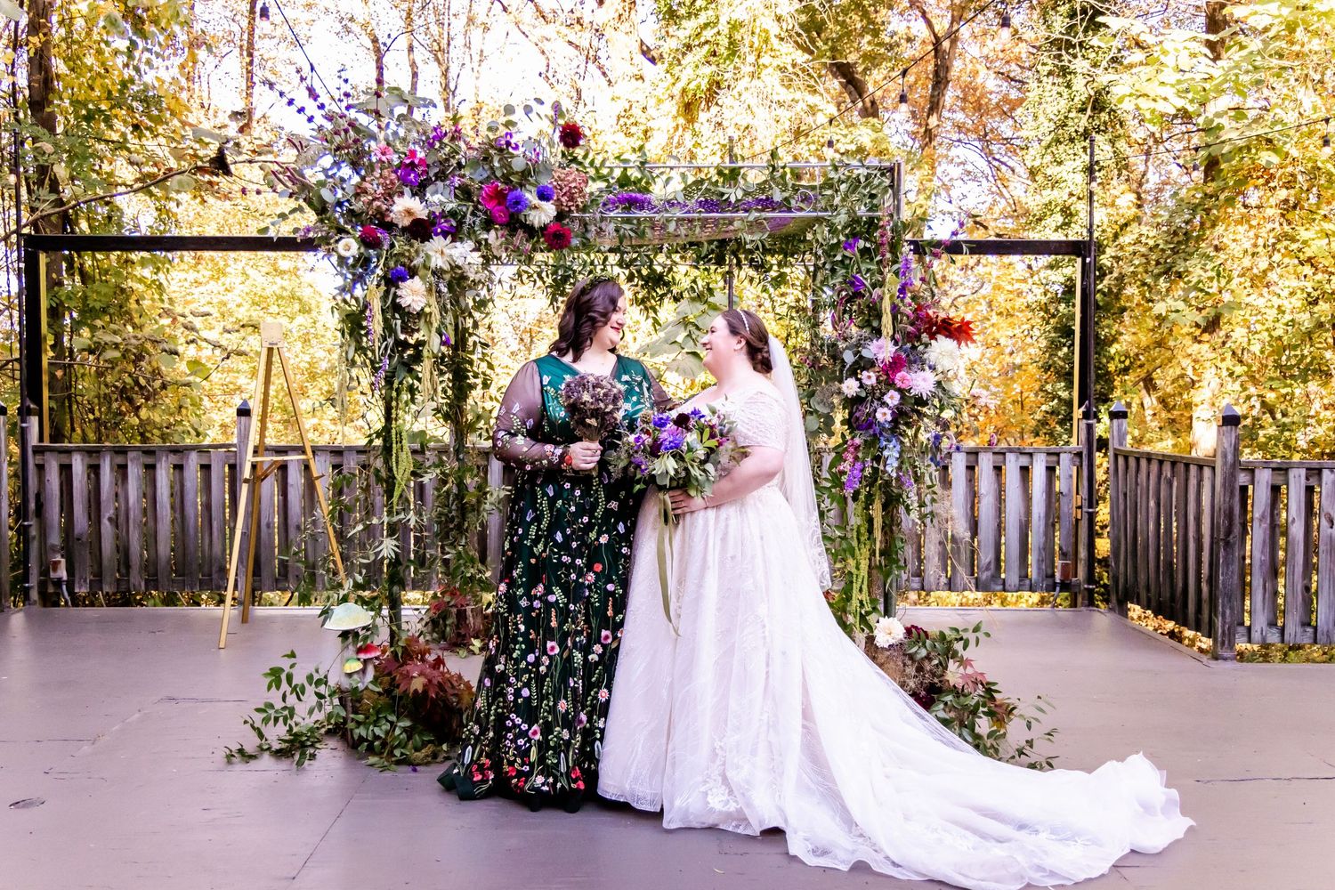 Wedding ceremony setup with floral arch and purple flower arrangements in an outdoor venue.