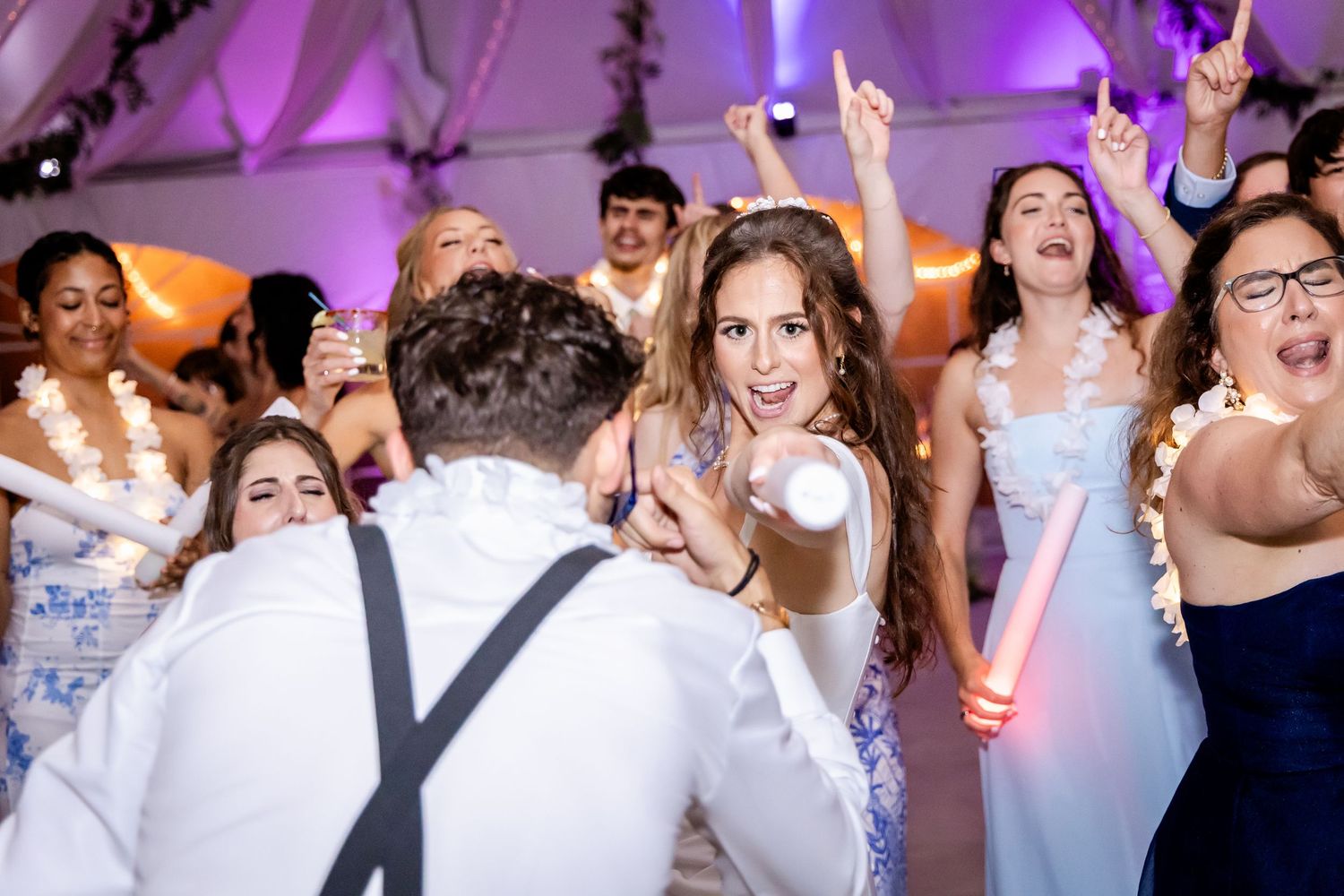 Wedding reception dance floor filled with guests under purple lighting.