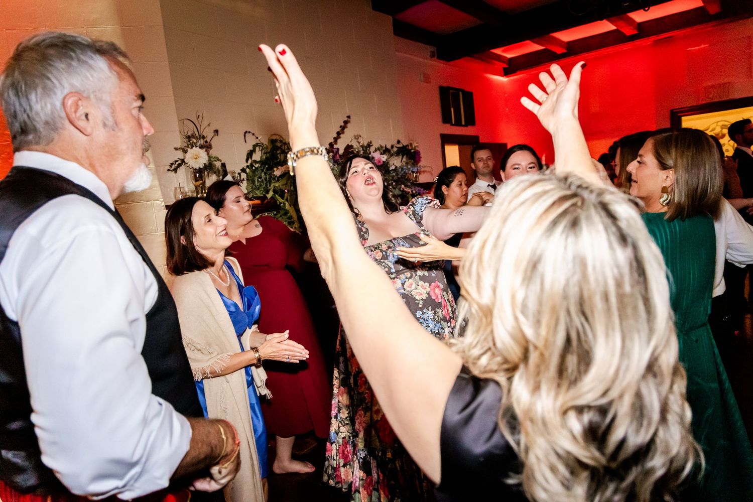 Wedding reception dance party with guests celebrating under red lighting.