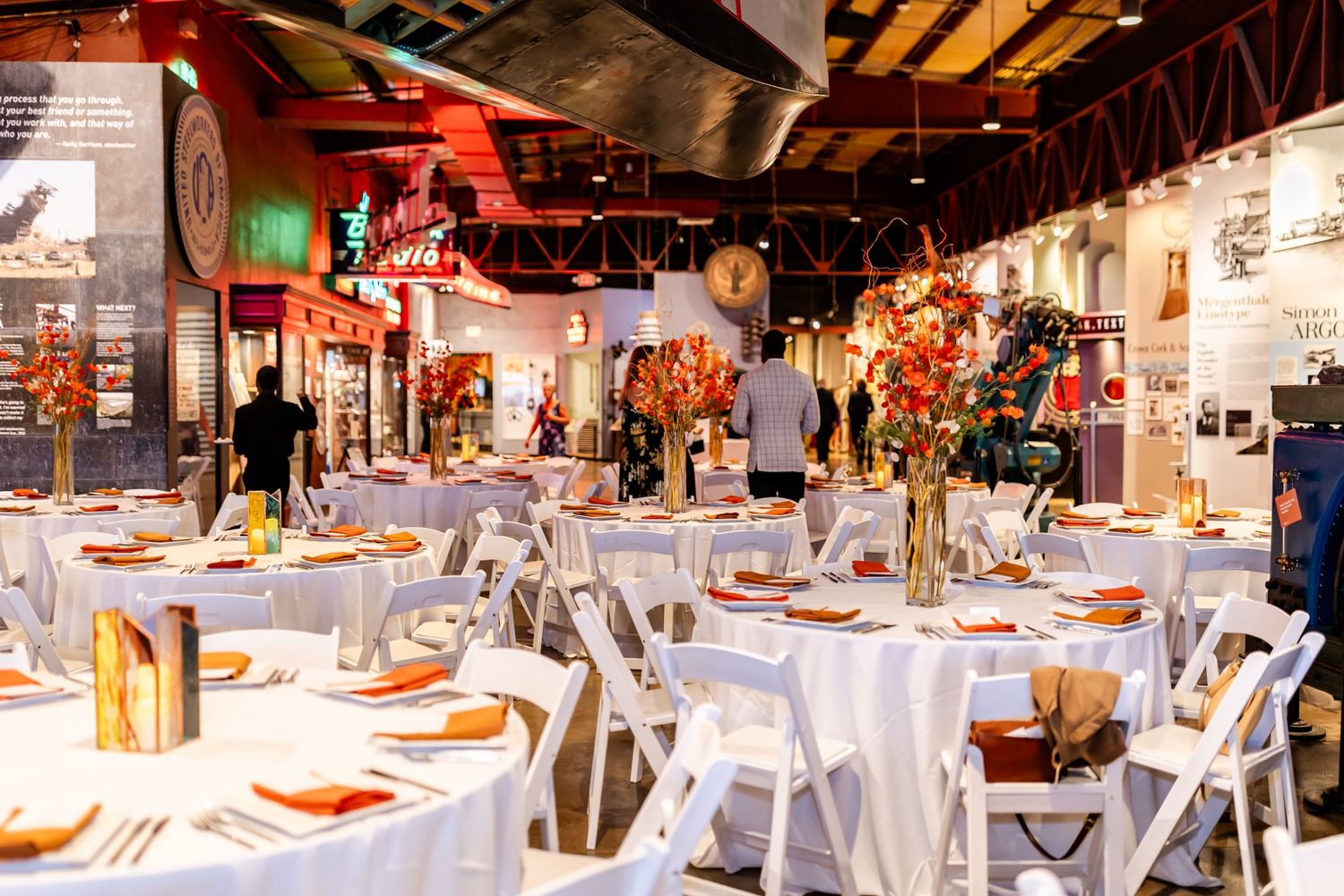 Wedding reception venue decorated with white tablecloths and floral centerpieces in an industrial-style space.
