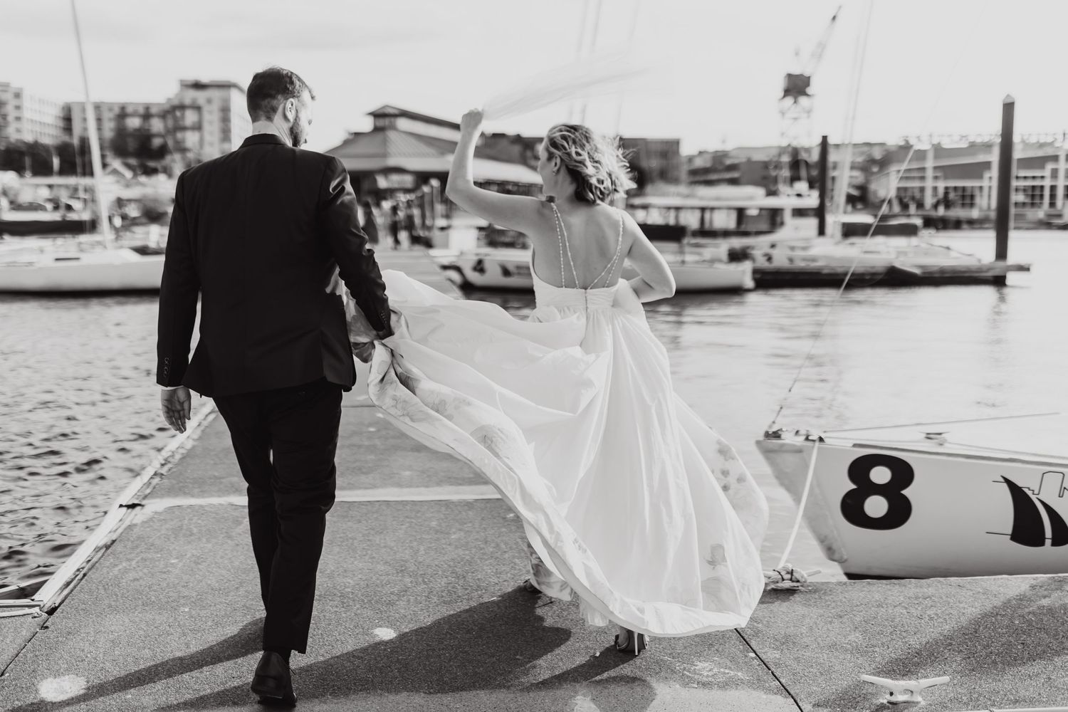 A couple walks along a marina dock as the bride's dress flows in the wind.