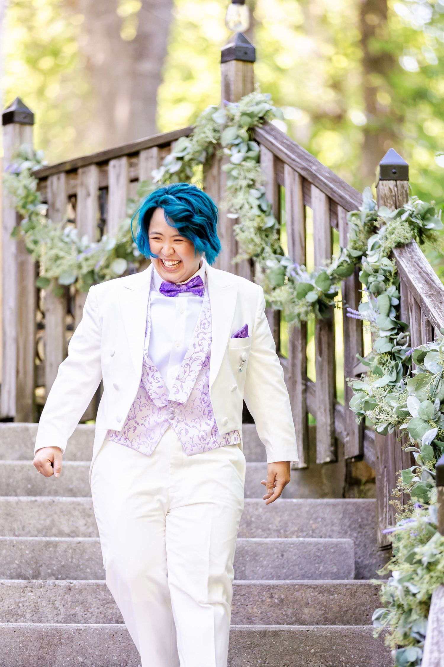 Person in white formal attire descends decorated wooden staircase with floral garlands.