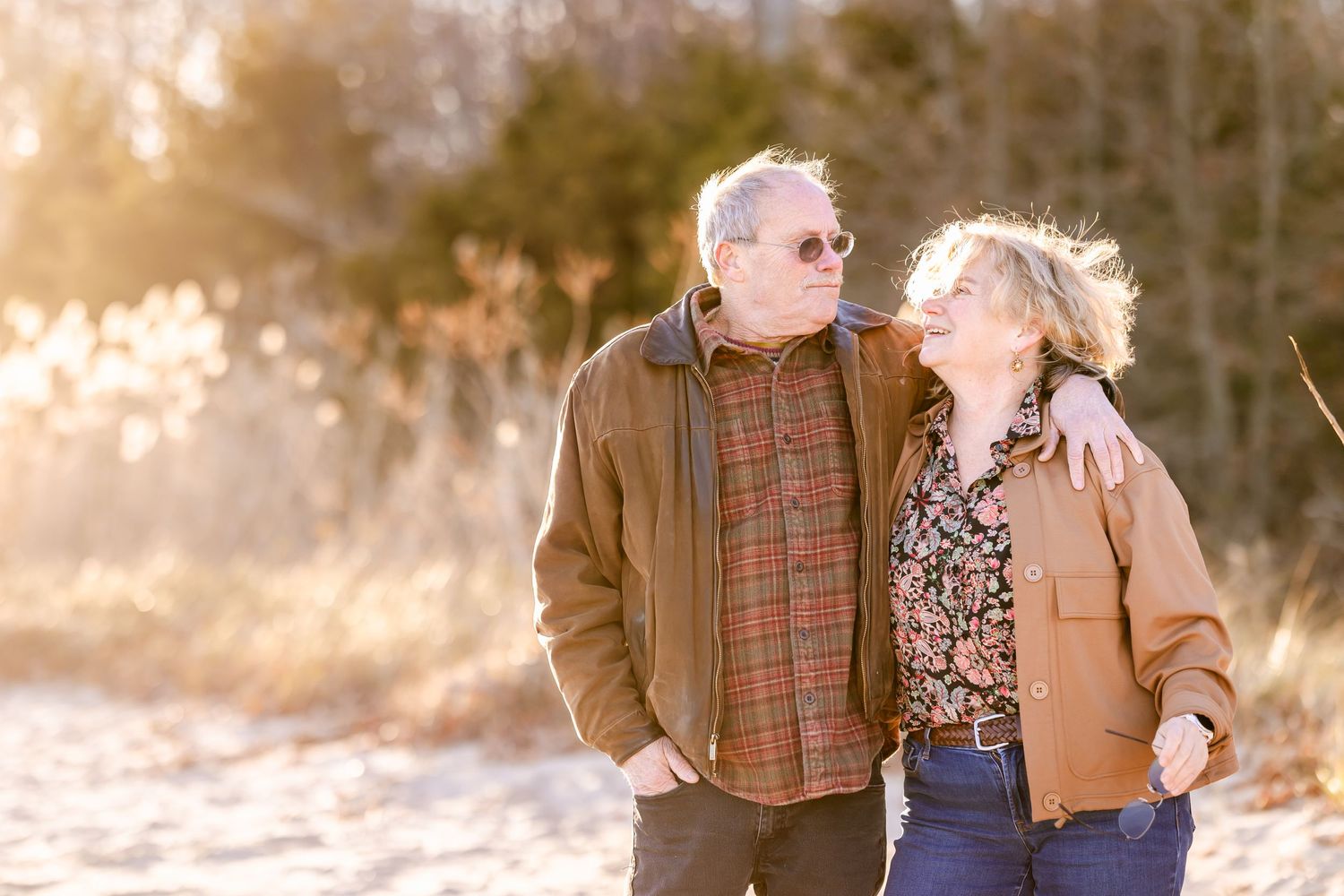 Senior couple in casual jackets shares intimate moment outdoors during golden hour.