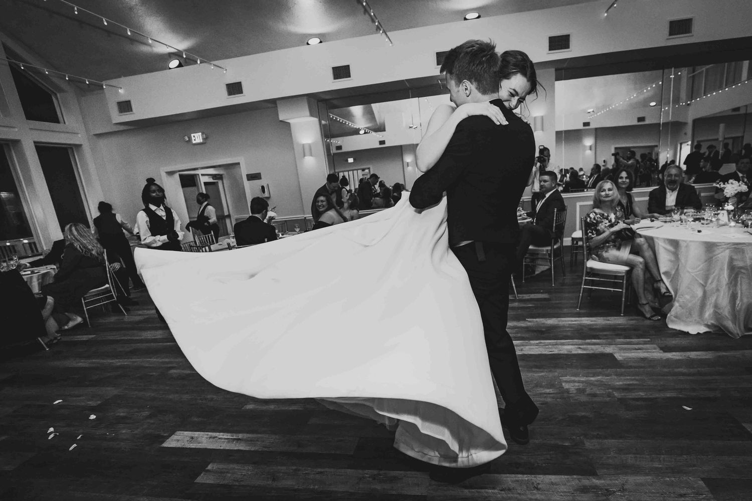A black and white wedding reception venue ballroom setup with elegant lighting and people gathered for celebration.