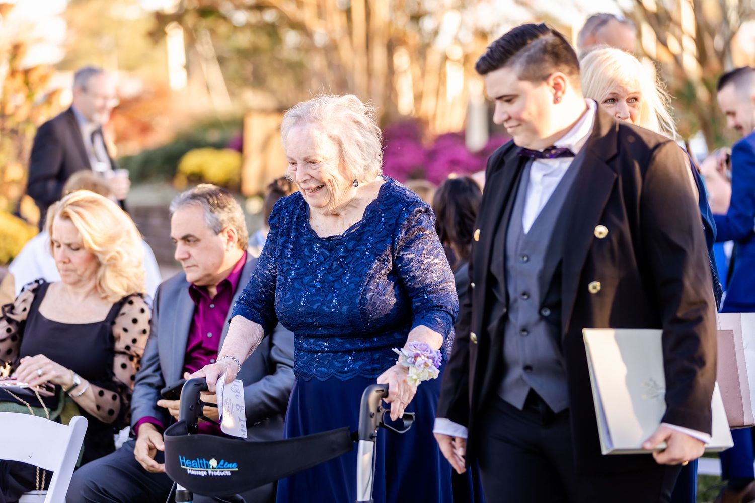 Event guests in evening attire gather on a garden path during sunset hours.