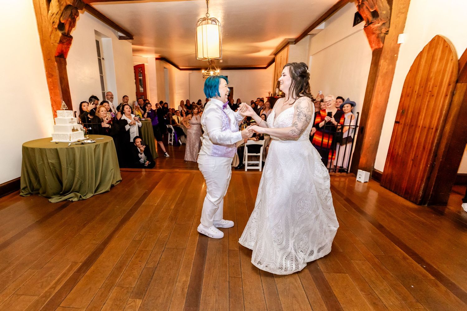 Dancing pair shares first dance at wedding reception on wooden dance floor surrounded by seated guests.