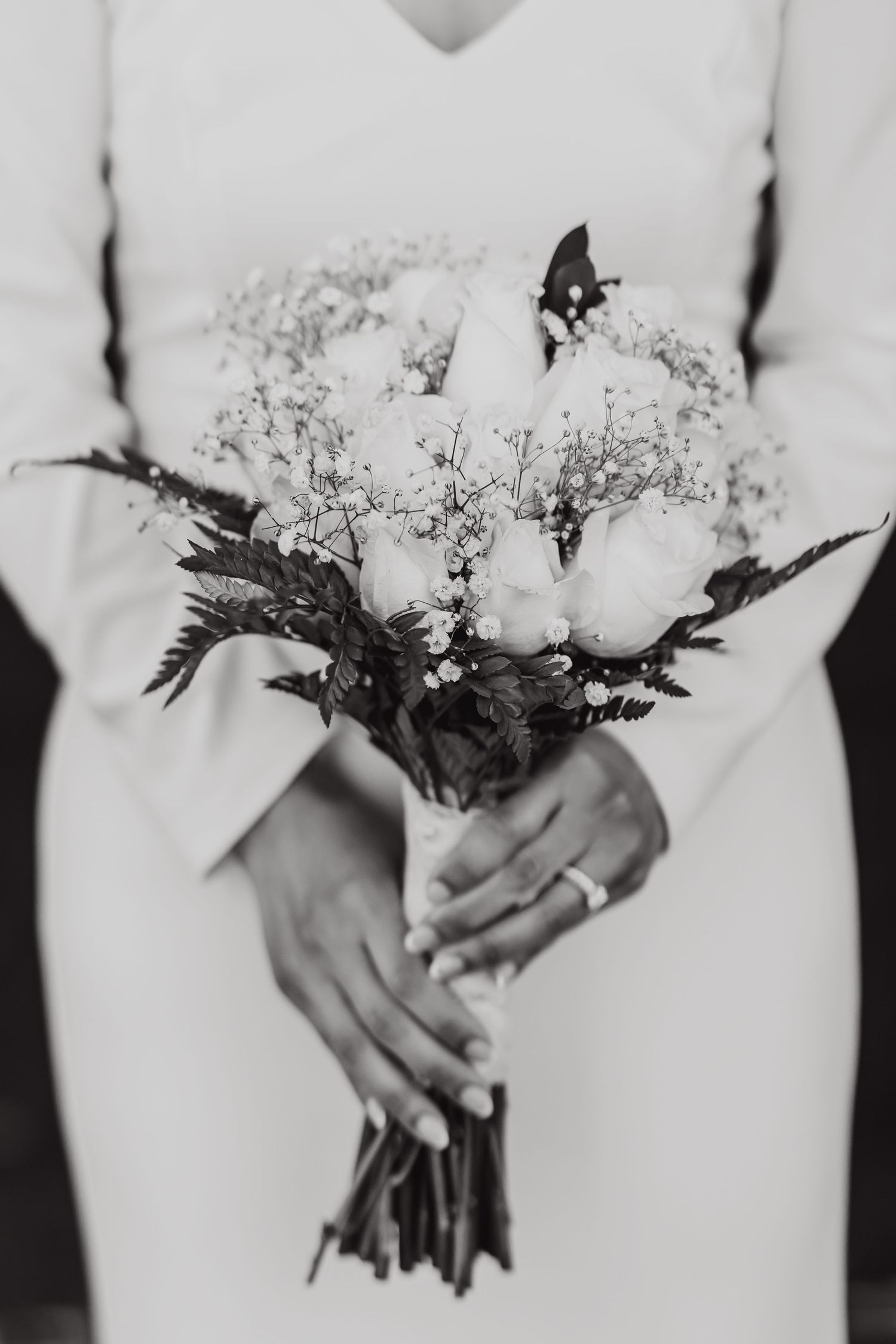 Black and white detail shot of hands holding a delicate floral bouquet with baby's breath.