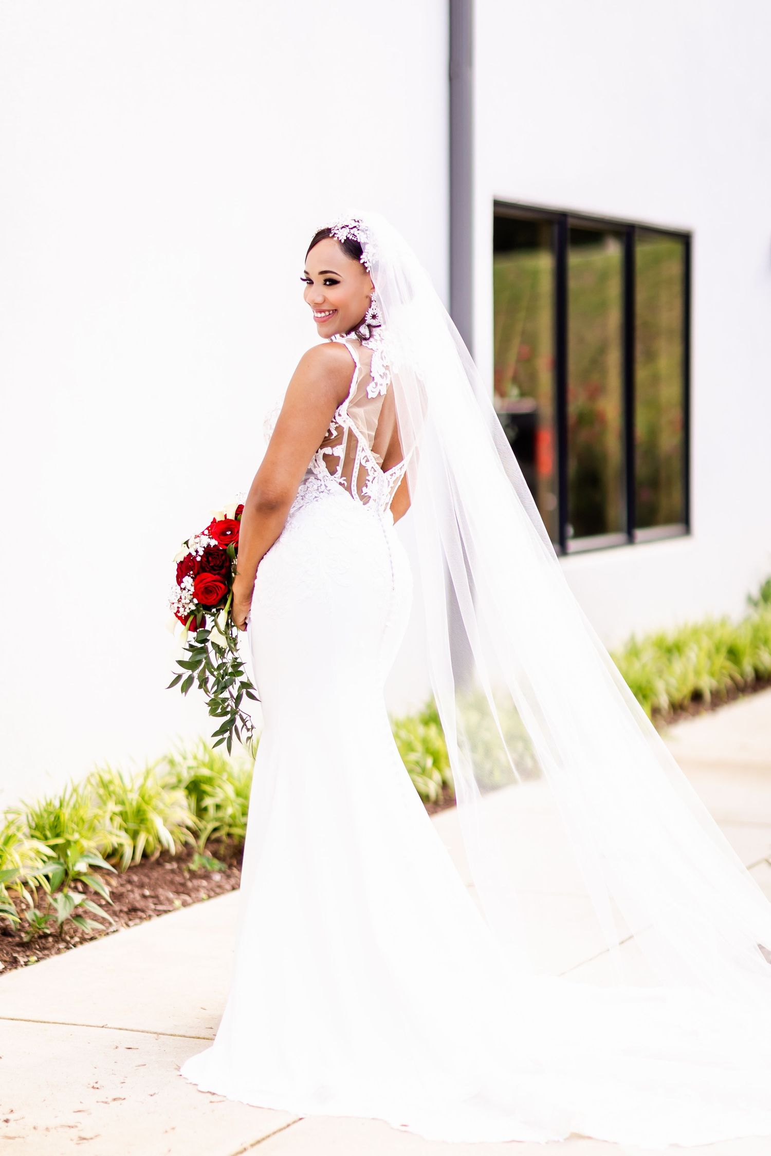 Full-length shot of a bride in a fitted white gown with long veil posing outdoors.