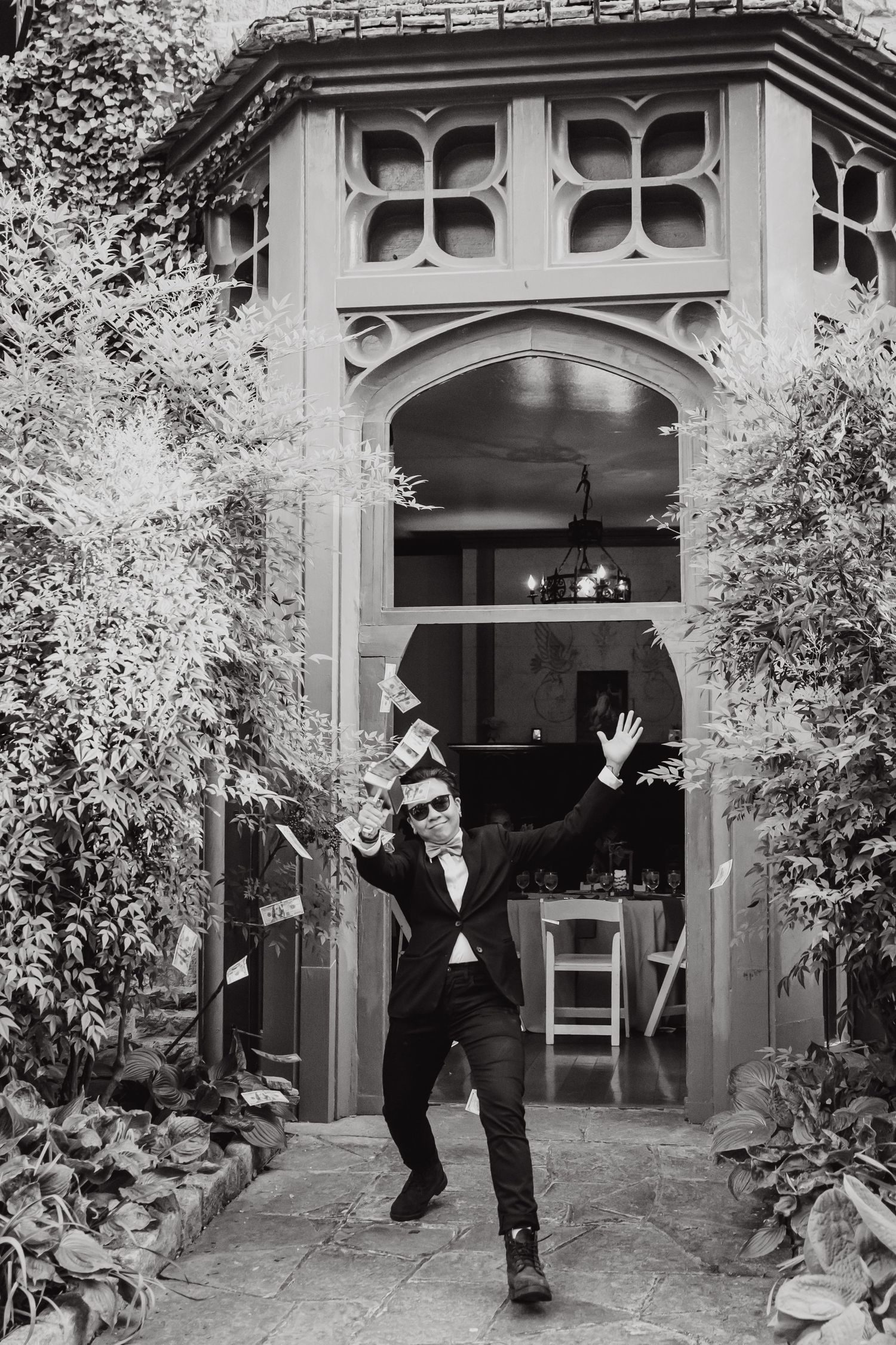 A black and white photo of someone jumping joyfully through an ornate garden archway.