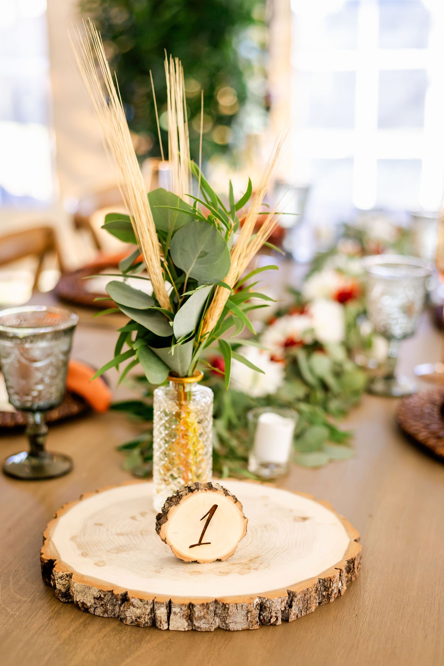Rustic wood slice centerpieces with table numbers and greenery arrangements on a wooden table.