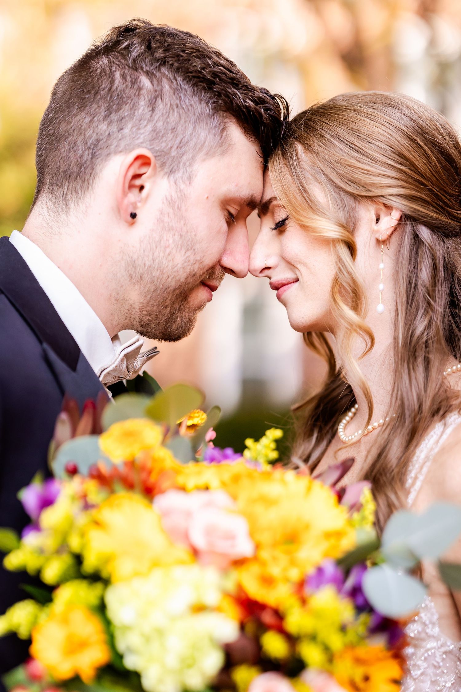 A romantic wedding couple shares intimate moments among vibrant yellow and purple flowers in a garden setting.