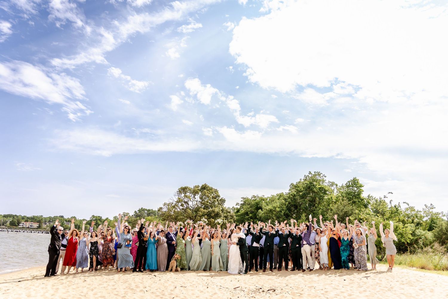 A large group of people gather outdoors under a bright blue sky for a group photo on a sunny day.