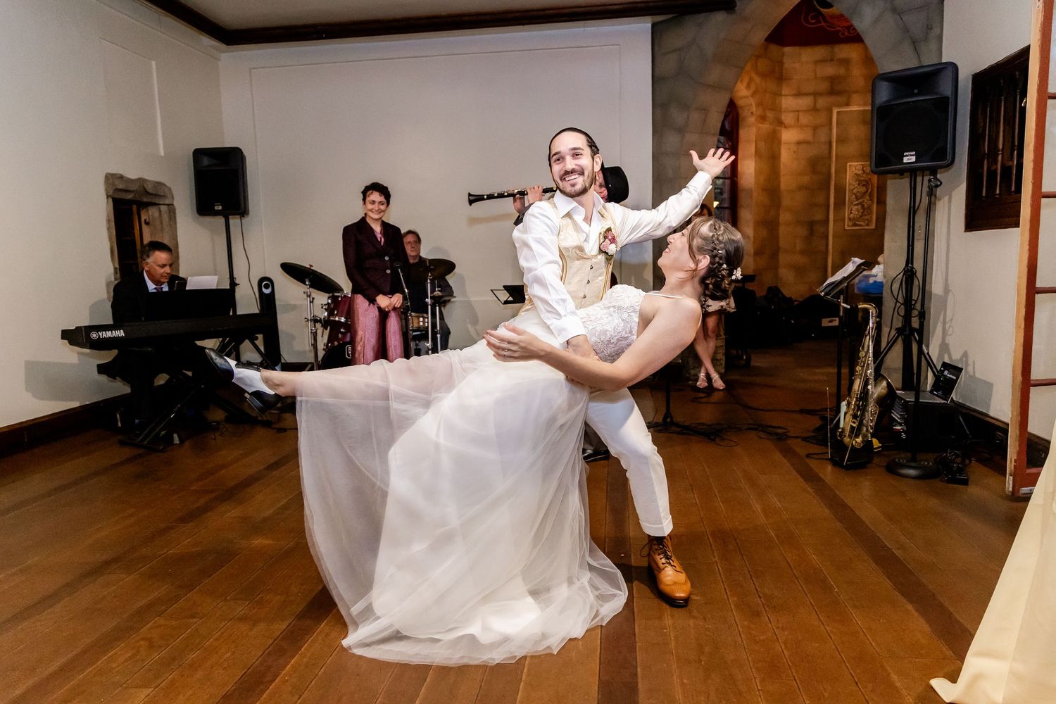 A bride and groom perform a dramatic dance dip during their first dance at a rustic wooden venue.