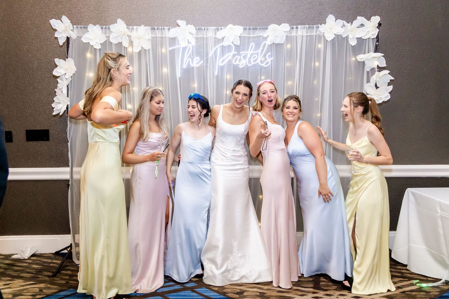 Wedding party posing in pastel dresses against an illuminated backdrop with neon signage.