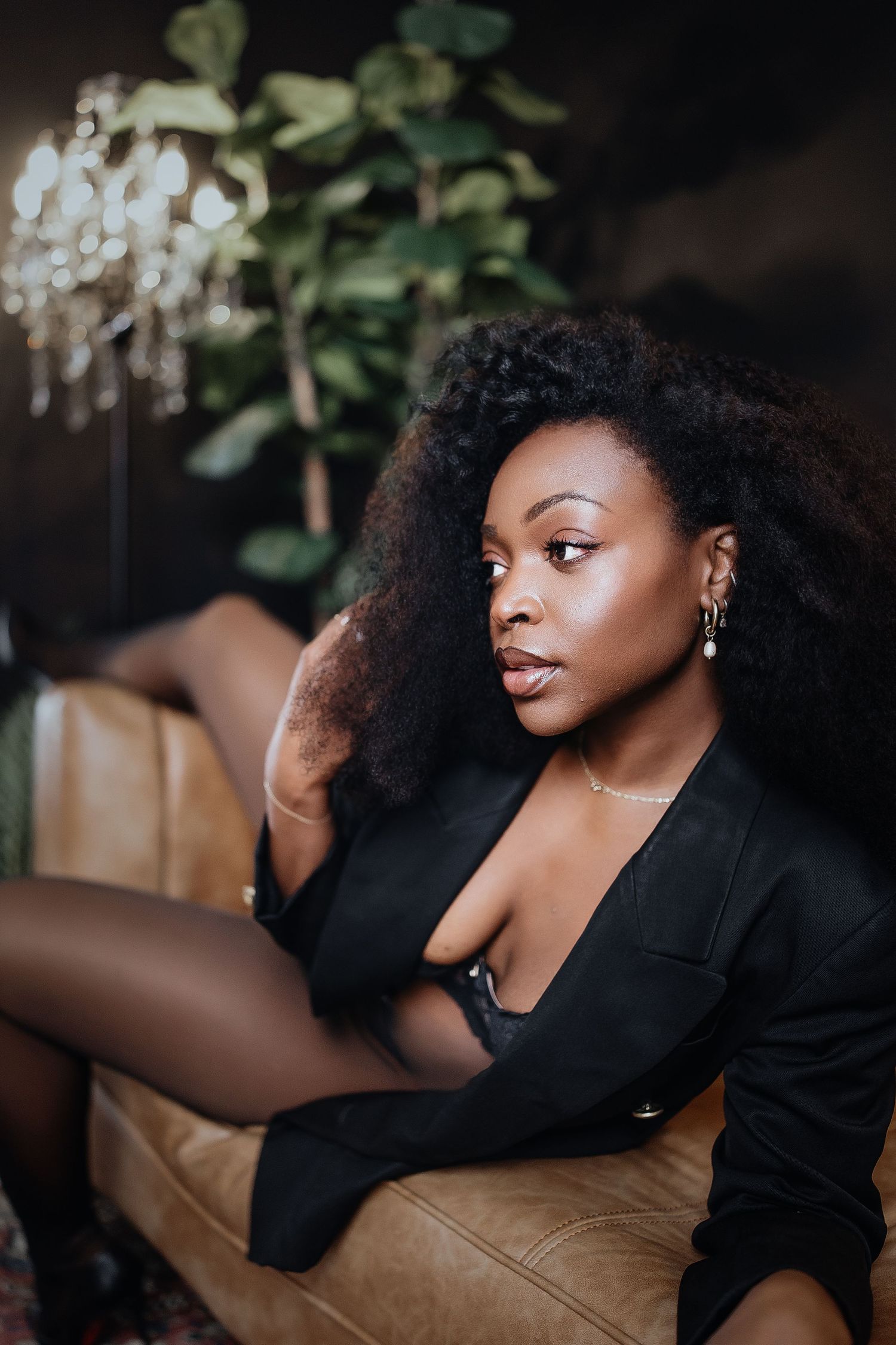 A person in a black outfit reclines on a brown leather couch in an artistic portrait series.