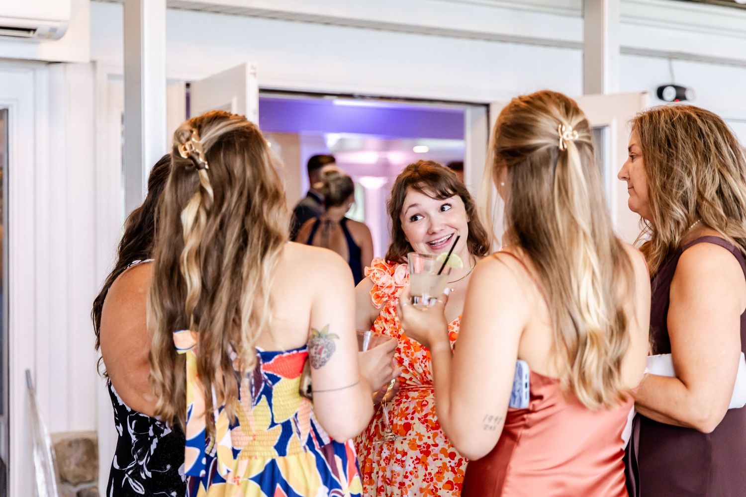 A group of wedding guests in colorful dresses laugh and chat during the reception.