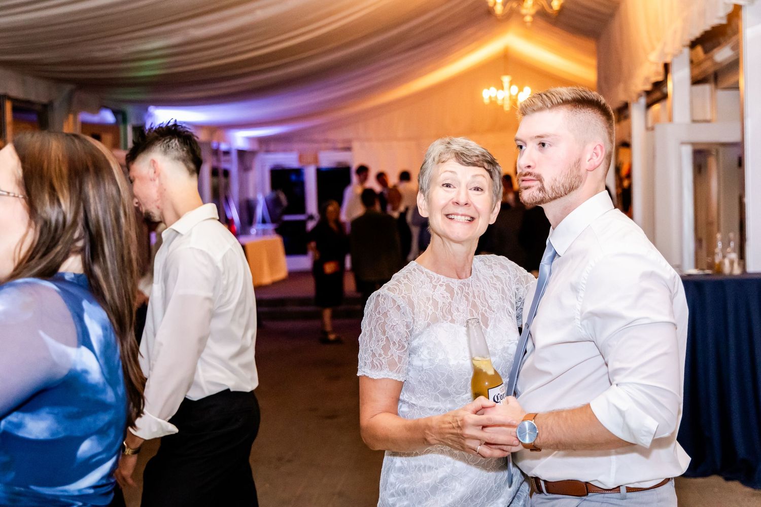 Reception venue with warm lighting and white ceiling drapes as guests dance and celebrate.