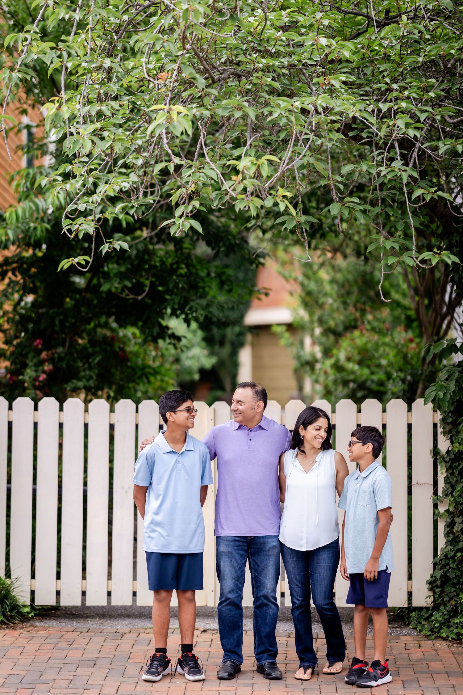 A group stands together in casual attire against a white picket fence surrounded by lush greenery.