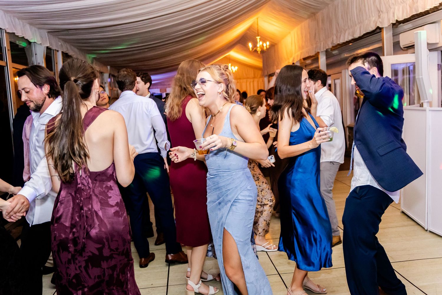 Wedding reception dance floor filled with guests under warm ambient lighting.