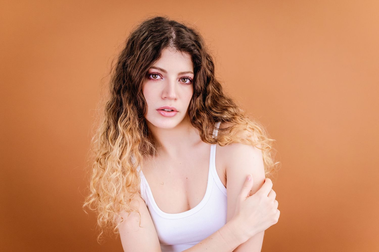 A sequence of studio portraits showing a model with curly hair in a white tank top against a peach background.