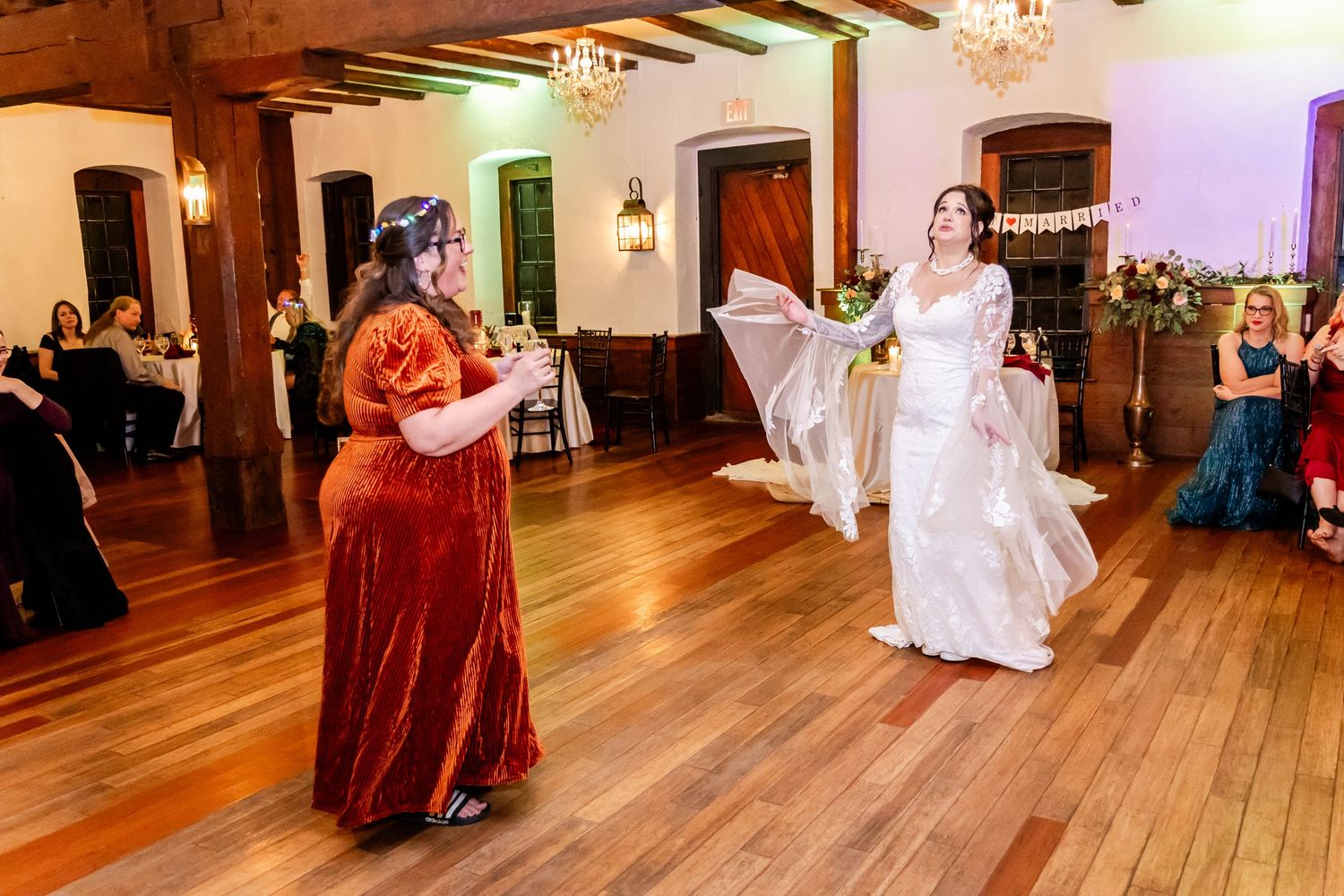 Wedding guests dancing on hardwood floors under rustic wooden ceiling beams.
