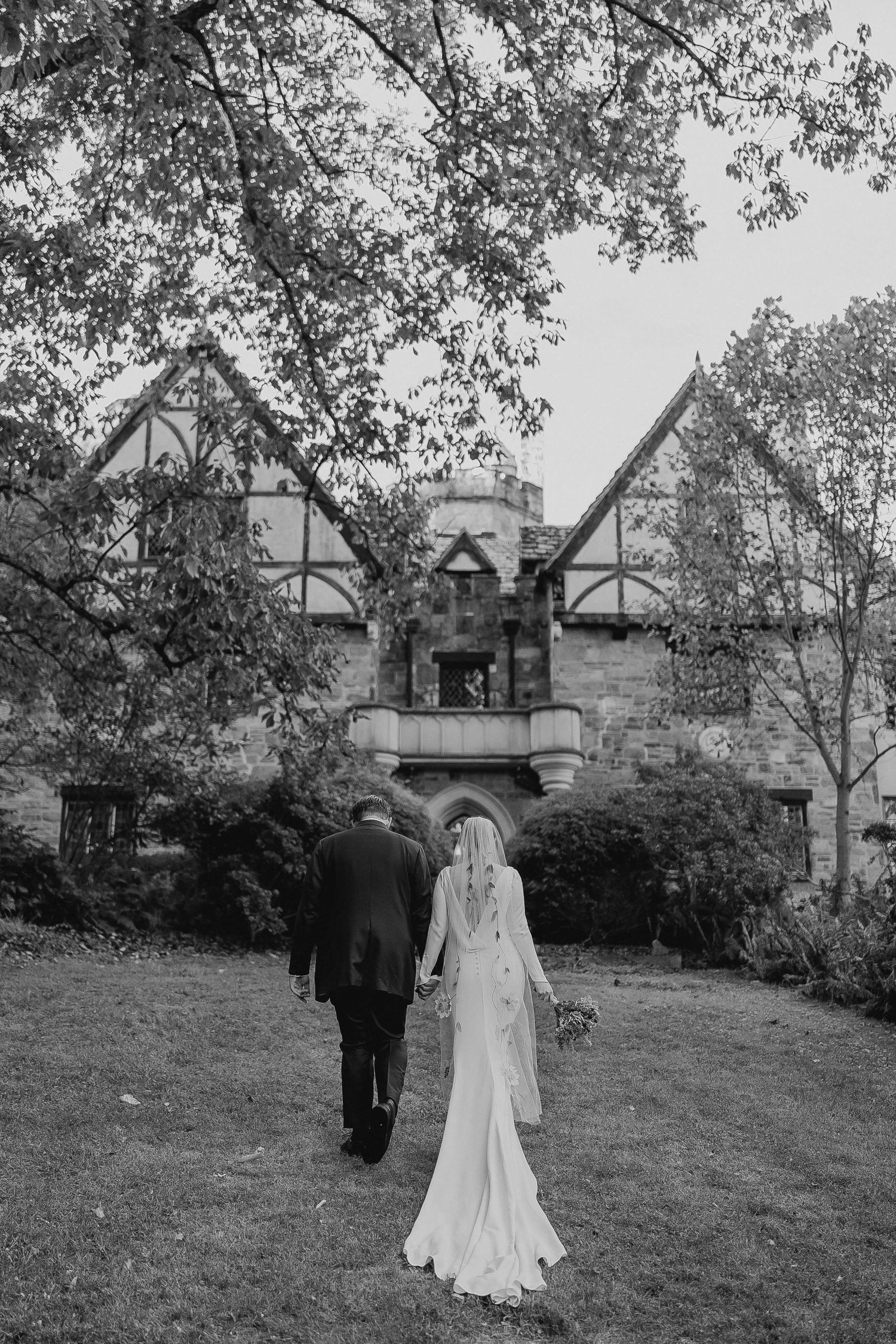 A black and white wedding photo sequence showing a couple walking away from a Tudor-style house in a garden setting.