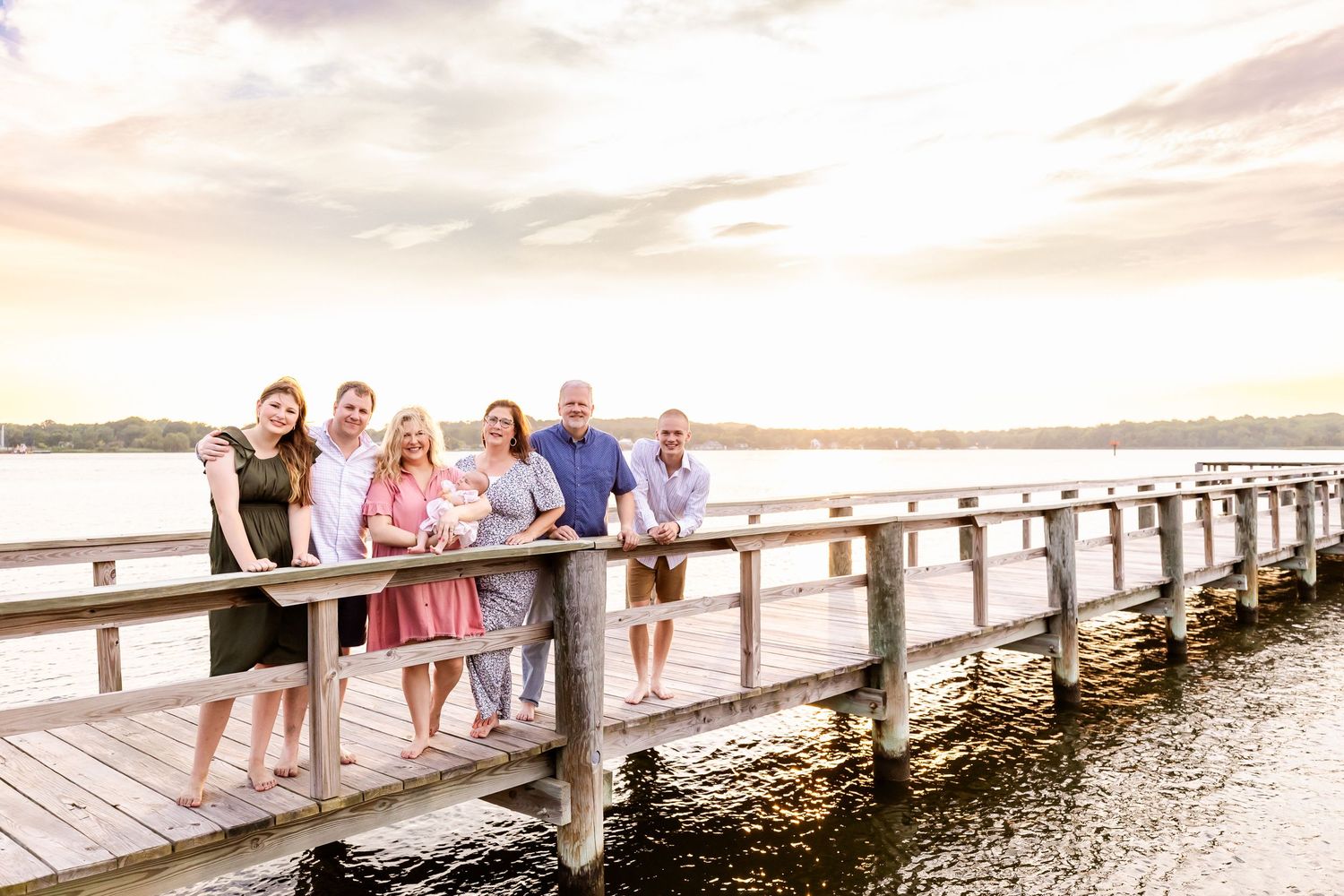 Family gathering on long wooden pier at sunset over peaceful lake.
