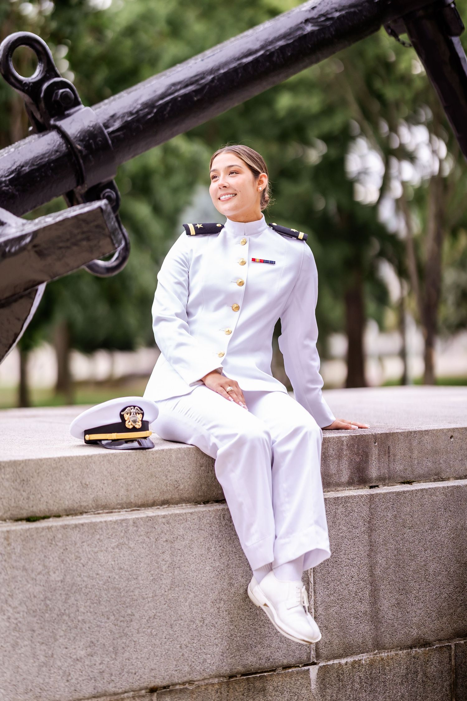Military officer in white dress uniform posing against a black cannon outdoors.