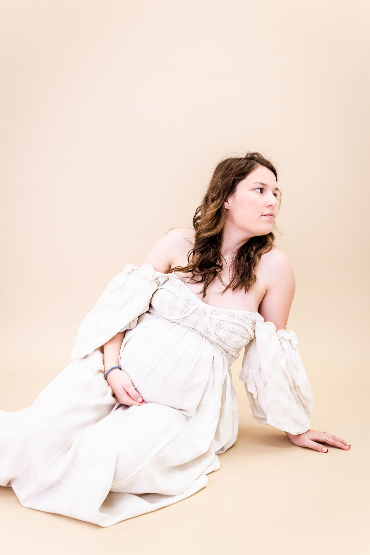 A serene maternity portrait with a woman in a white dress against a neutral backdrop.