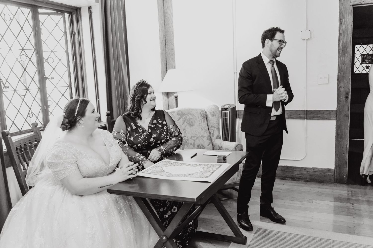 Wedding ceremony participants gathered around a table signing documents in an indoor setting.