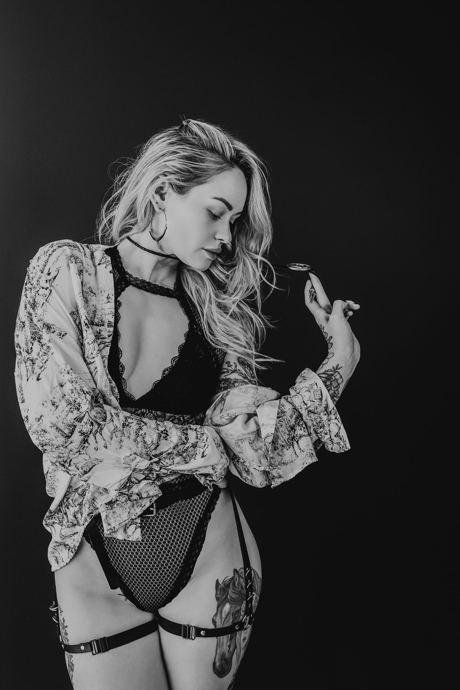 Black and white boudoir portrait featuring a woman in lace lingerie and flowing floral robe posing artistically.