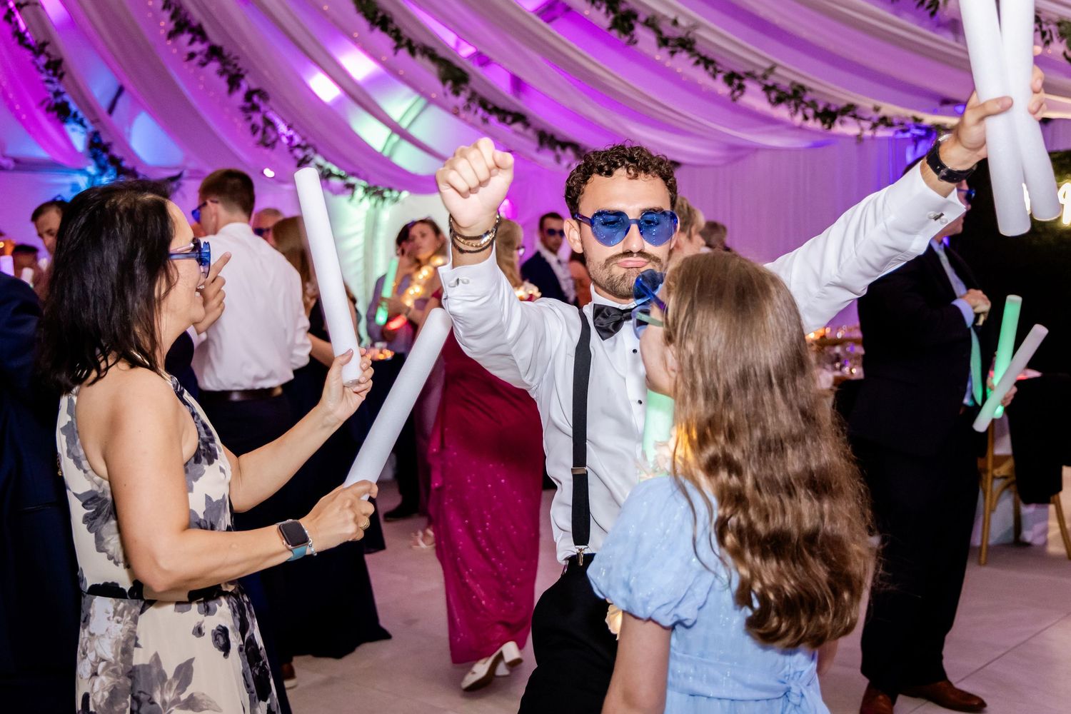 Energetic dance party with guests celebrating under purple mood lighting and draped fabric decor.