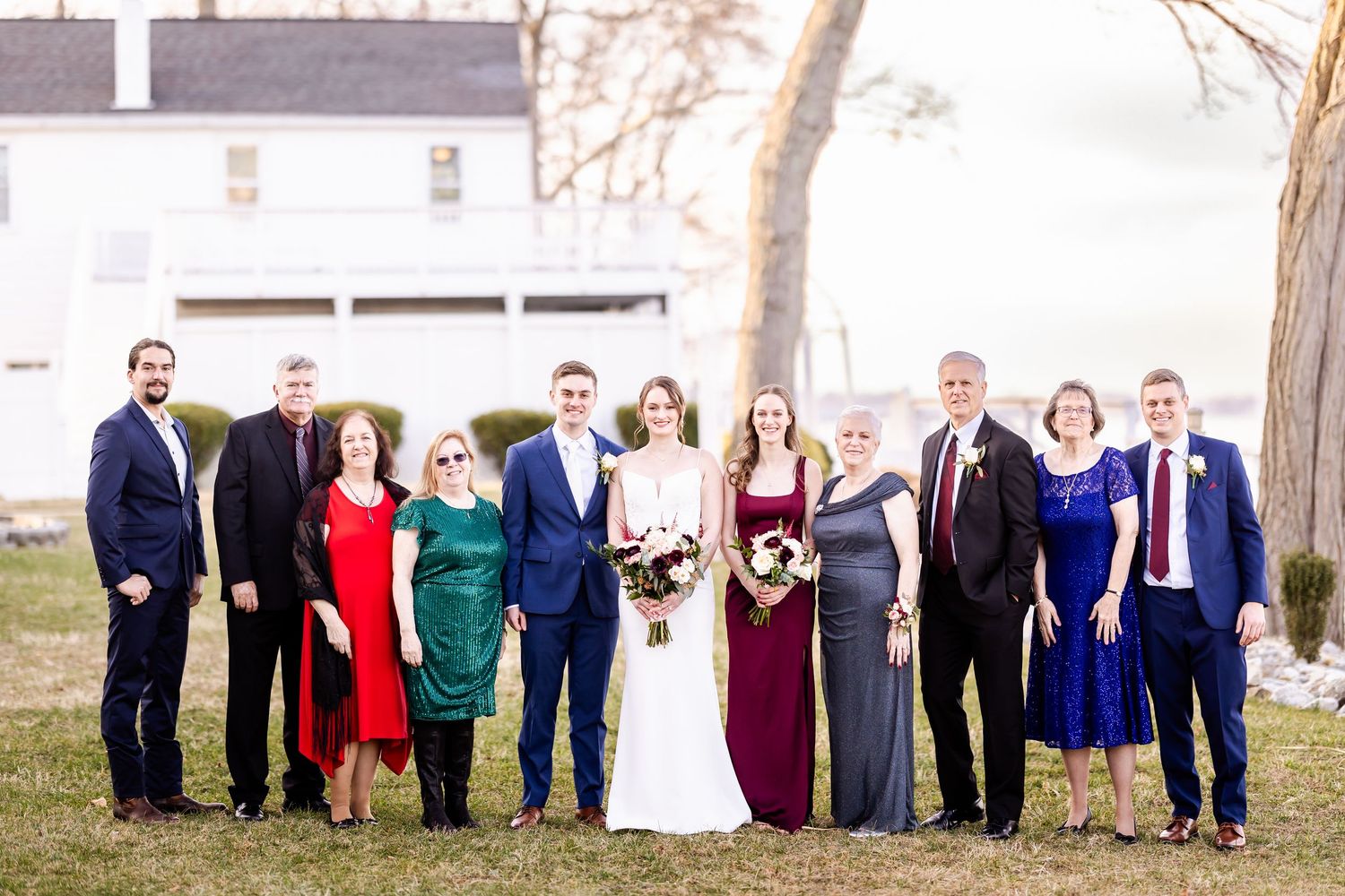 Large wedding party group photo with people wearing formal attire in various colors outdoors.
