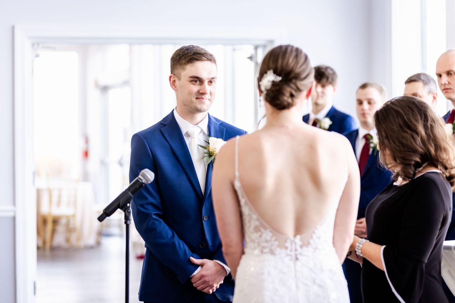 Wedding guests and party members socializing in an elegant white room with natural lighting.