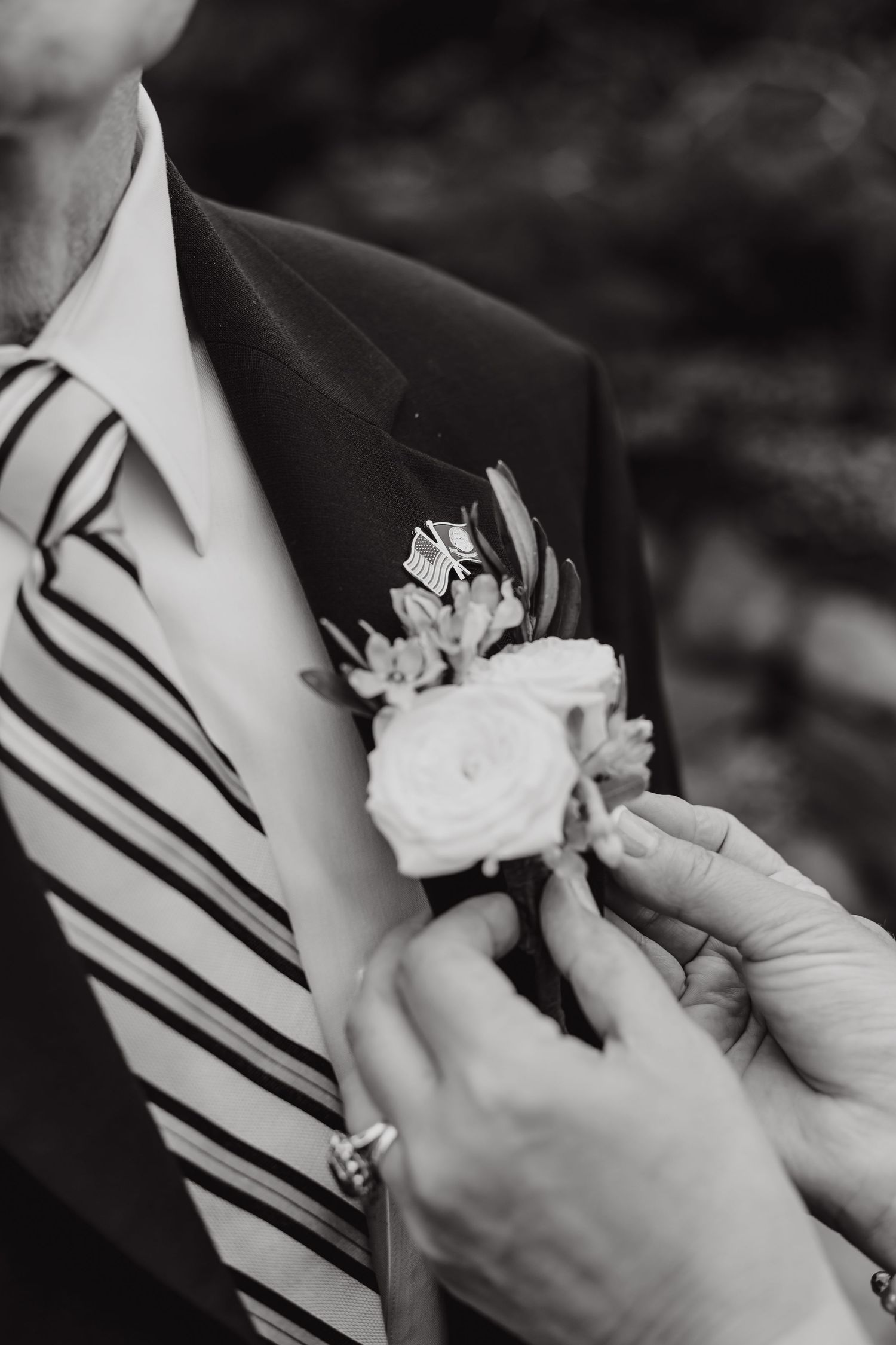 Close-up black and white shots of hands pinning boutonniere on lapel.