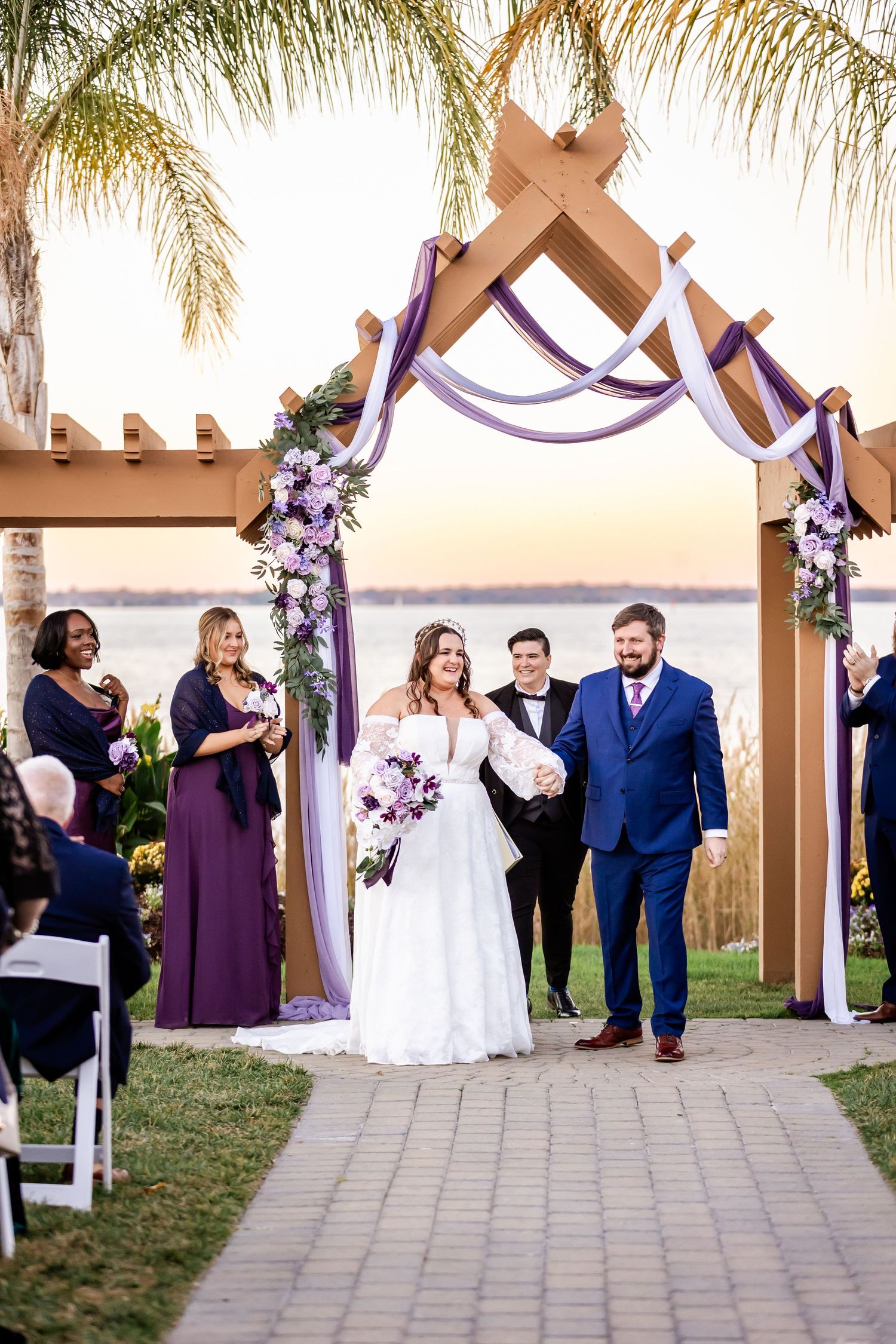 Wedding ceremony exit under cross-adorned arch with purple draping and palm trees.
