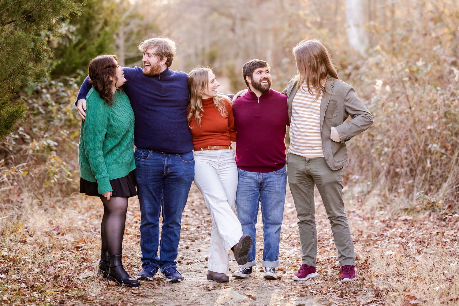 Five people standing casually together and smiling on a wooded autumn path.