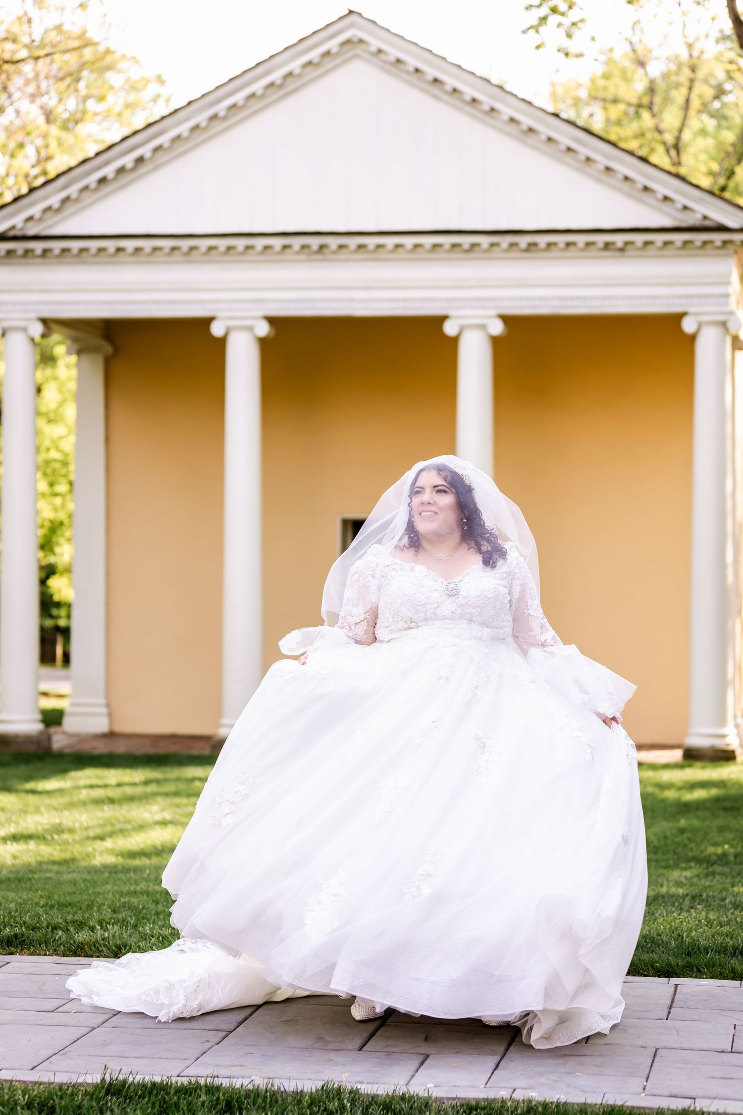 Bride in flowing white dress twirls joyfully in front of classical columned building.