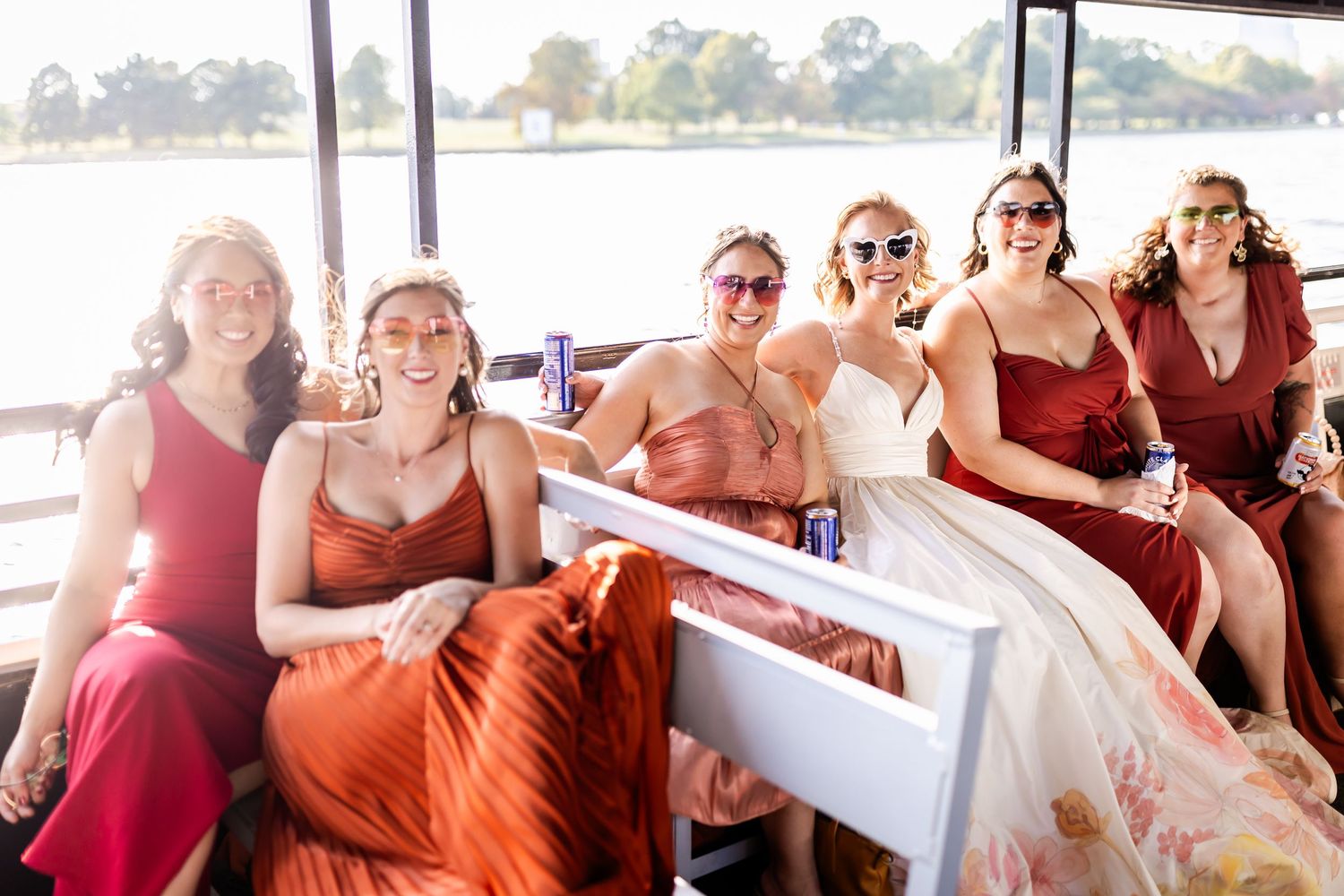 A group rides together on a boat wearing formal red dresses and enjoying the sunny day.