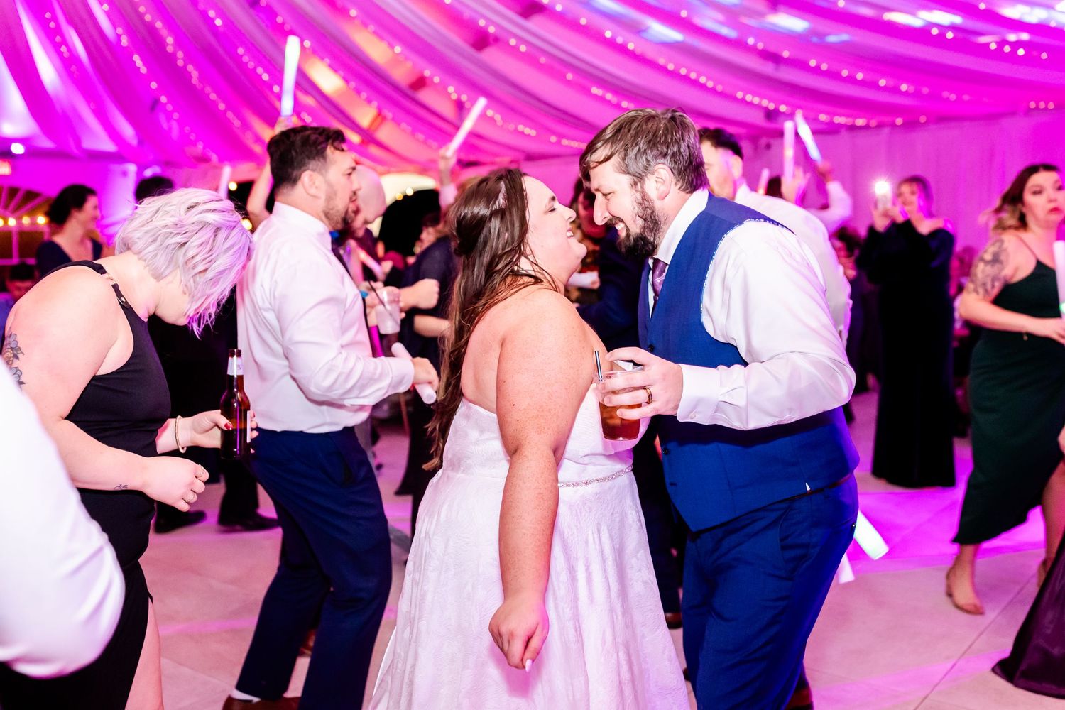 Wedding celebration with guests dancing under pink-lit fabric draped ceiling.