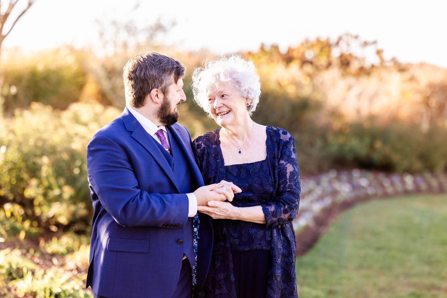 A tender moment shared between a couple in formal attire against a sunset backdrop in an outdoor garden setting.