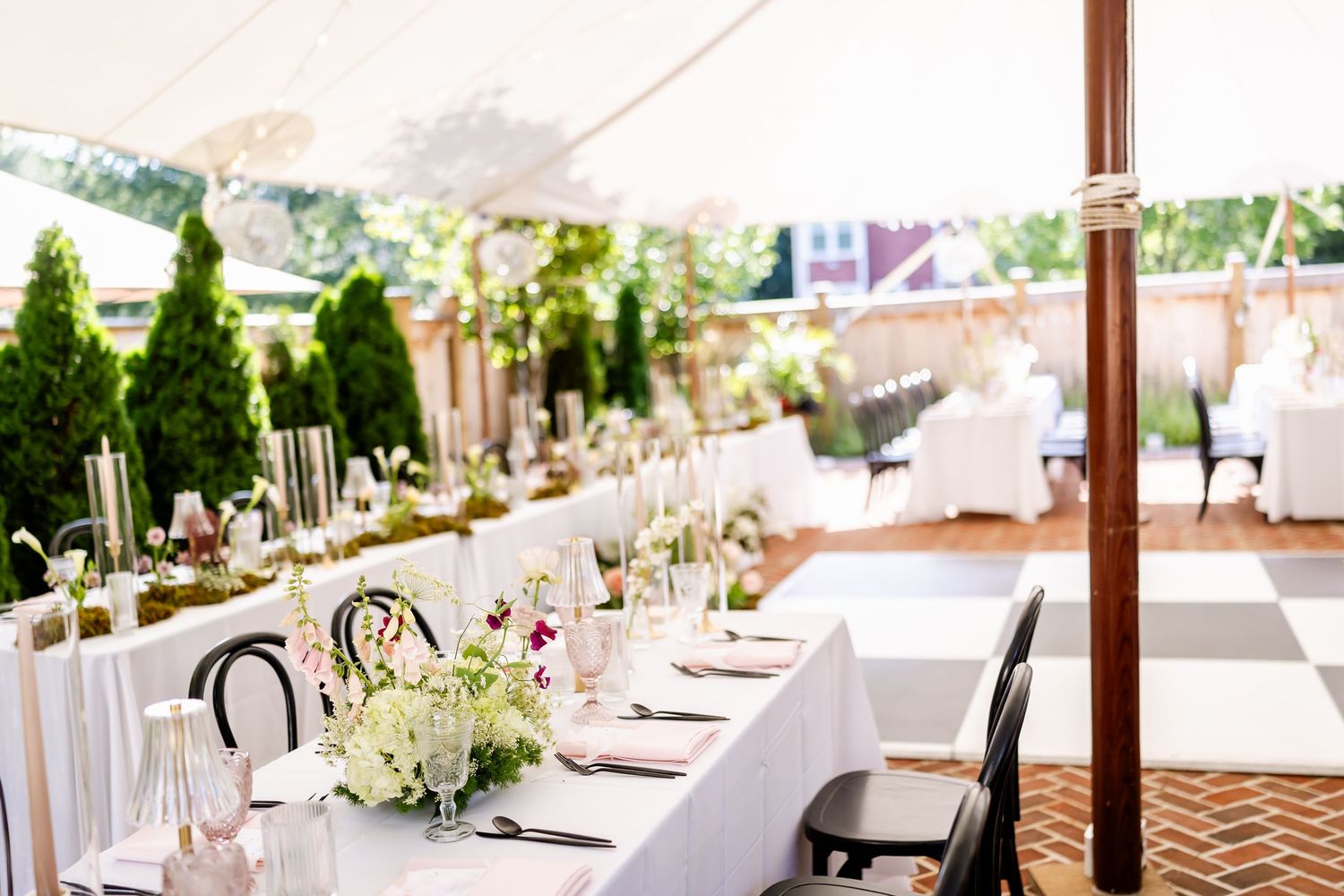 Elegant wedding reception table setup with white linens and floral centerpieces under an outdoor tent.