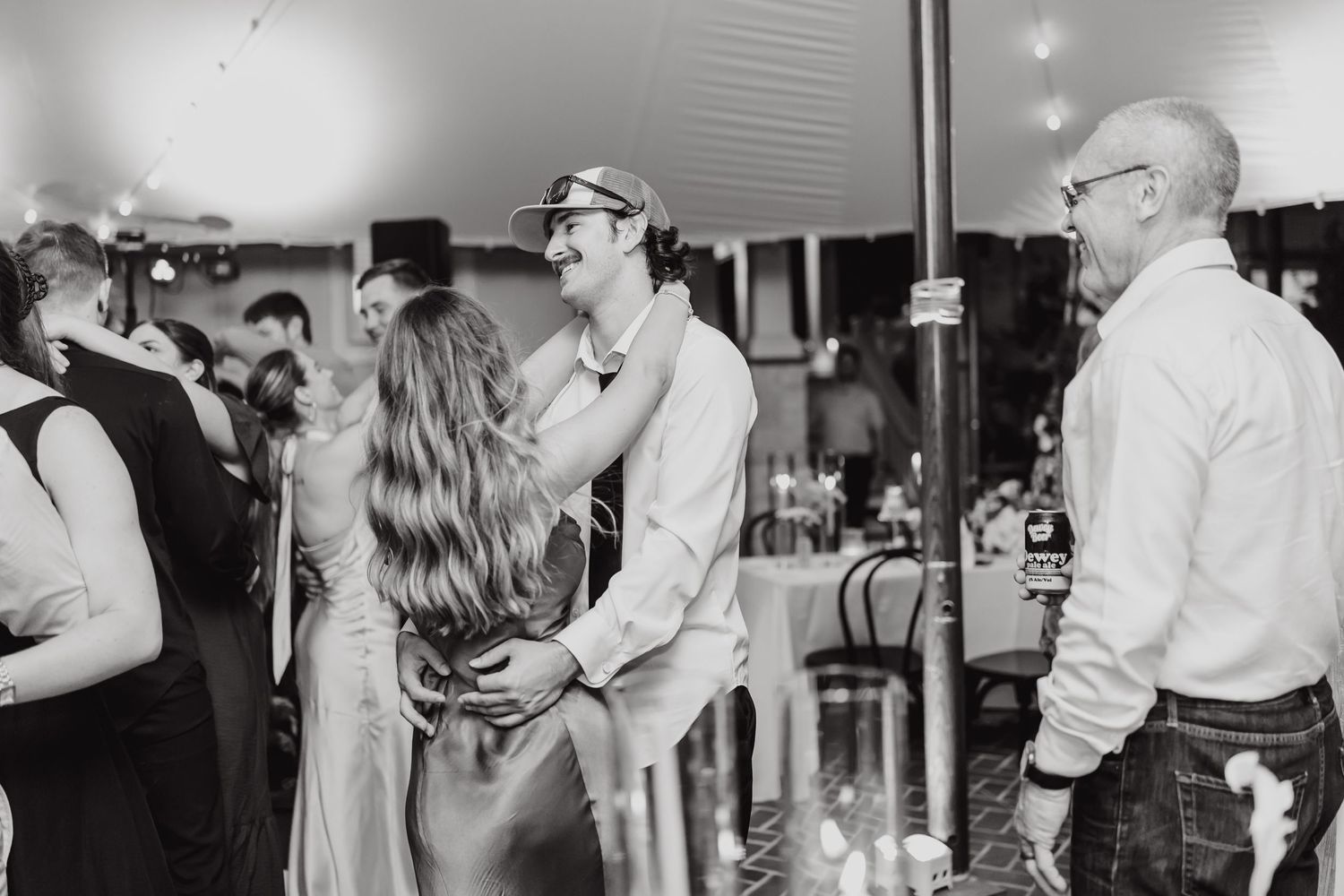 Wedding guests dance and celebrate on a lively dance floor at an indoor reception.