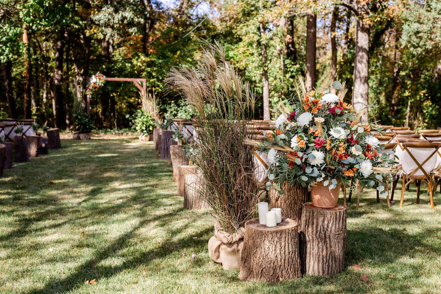Rustic outdoor wedding venue decorated with wooden log stands and floral arrangements.
