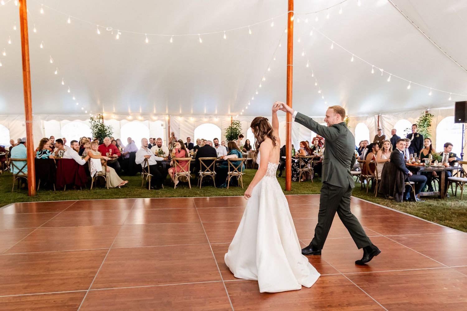 Couple performs their first dance under string lights in an elegant white tent reception.