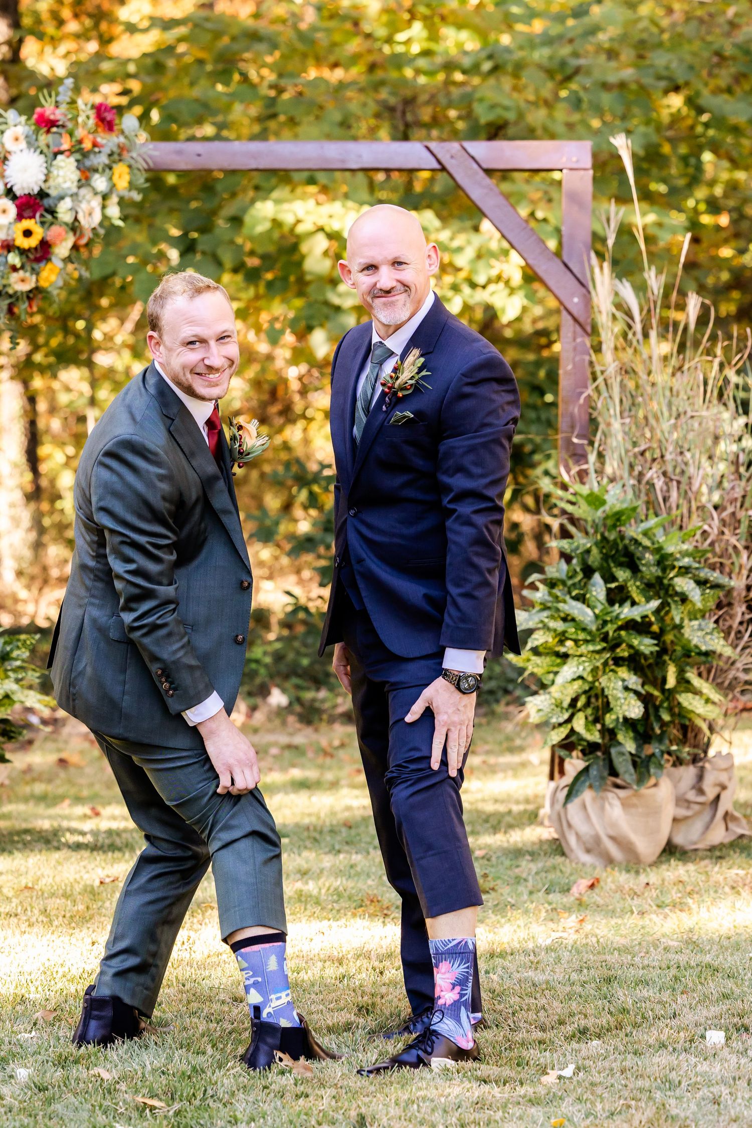 Groomsmen show off colorful socks in playful outdoor wedding photo.