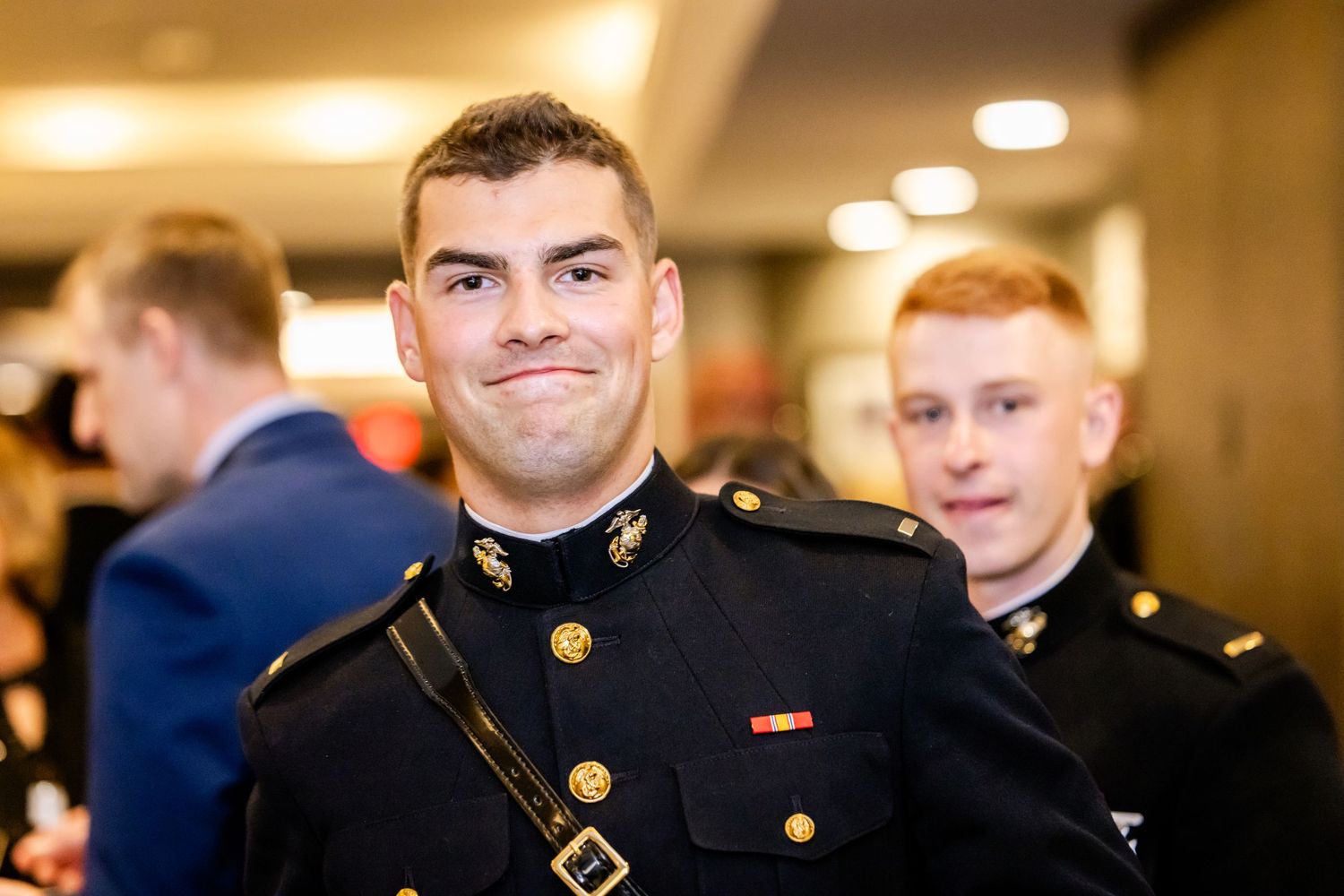 Military officers in formal dress uniforms stand together at an indoor event.