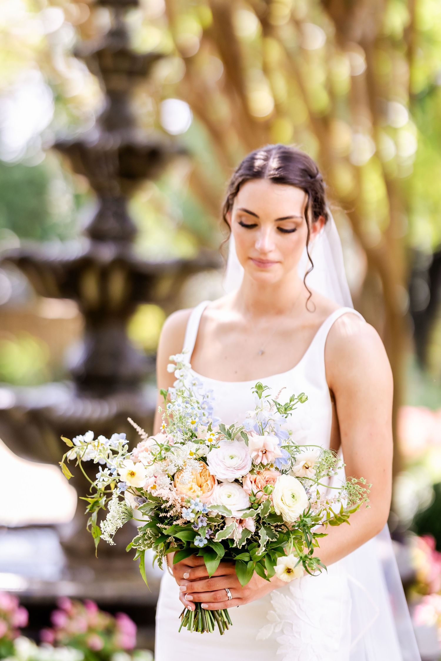 Bride holding delicate bouquet of white and pink flowers in outdoor garden setting.