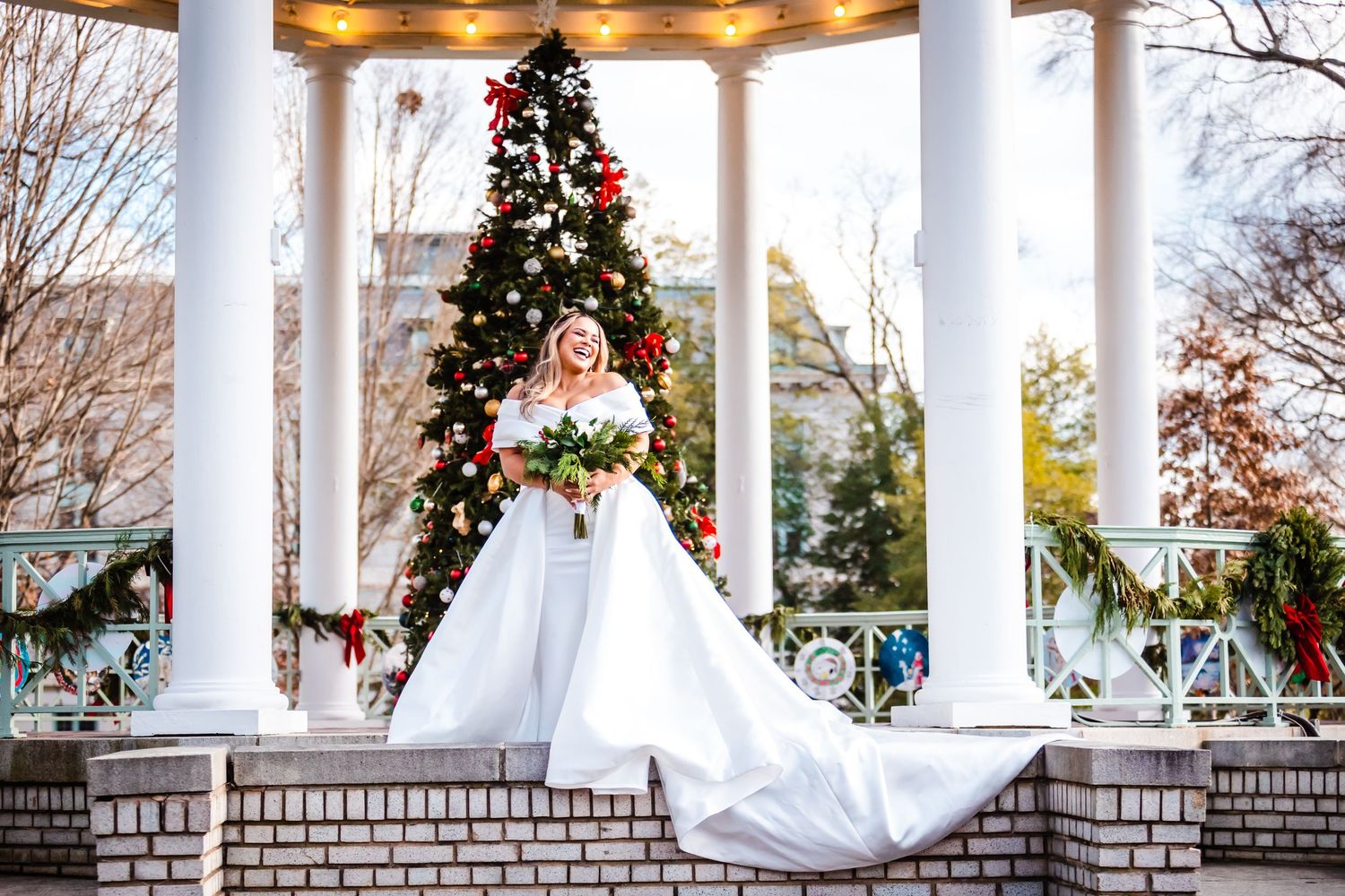 A white gazebo decorated with Christmas wreaths and garland stands elegantly against a winter landscape.