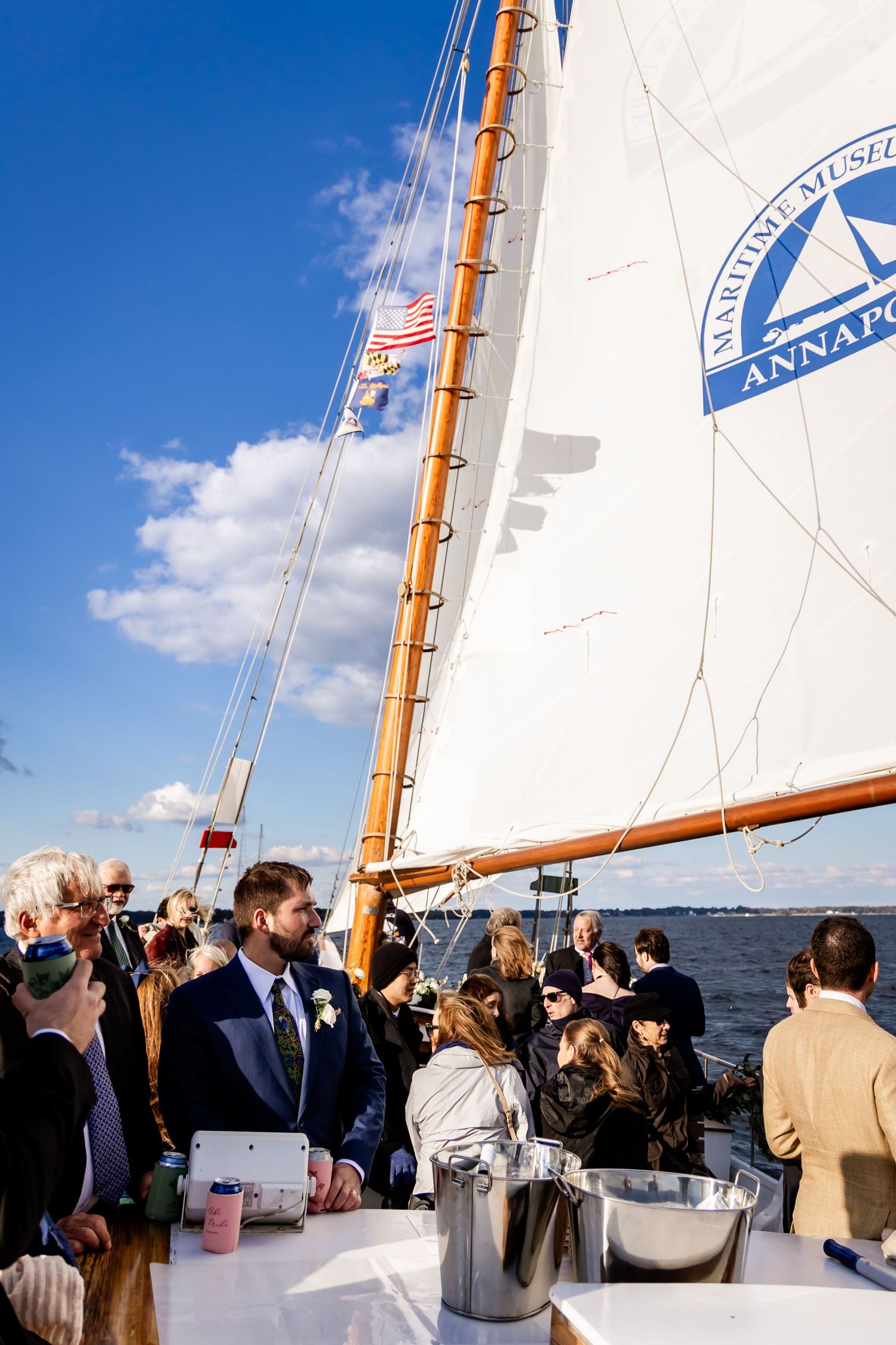 Wedding ceremony on a sailboat at Annapolis Maritime Museum with guests gathered under white sails on a sunny day.